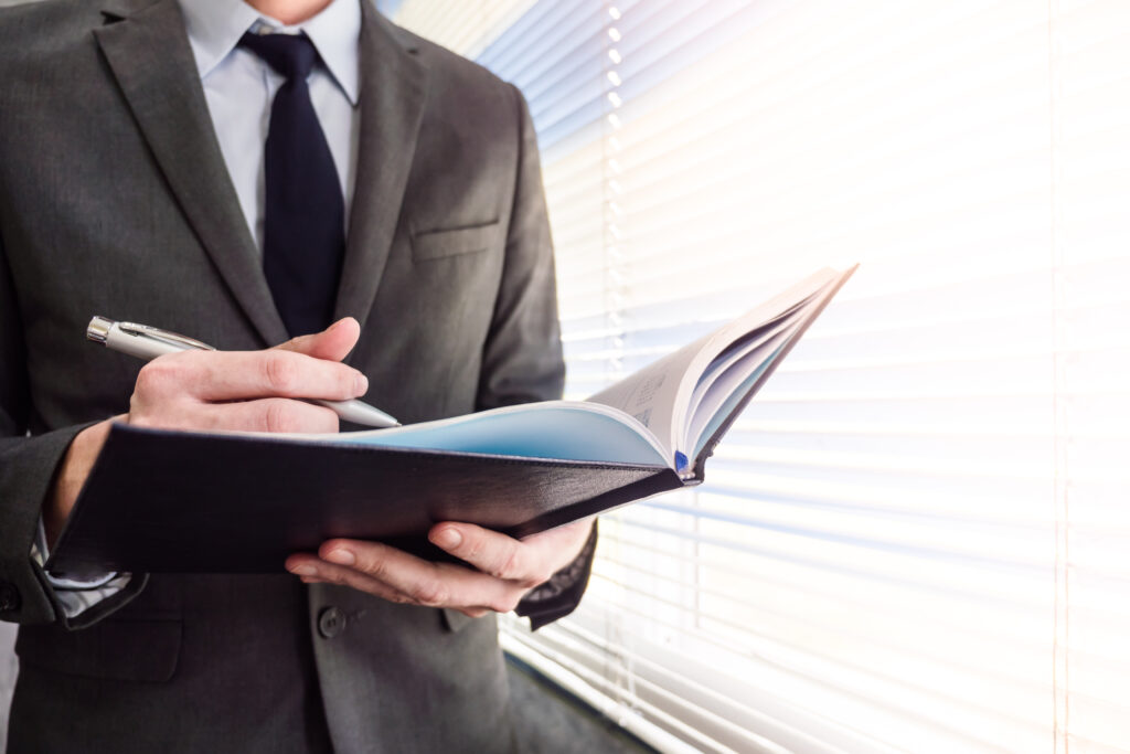 A male paralegal standing by the window with a notebook and pen in hand.